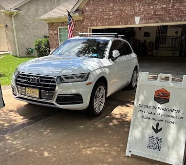 White Audi Q5 being detailed in a customer's driveway with a Texas Auto Club Detail In Progress sign displayed